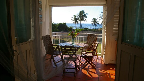 Un balcón con mesa y sillas, con vista a una playa con palmeras y el océano.