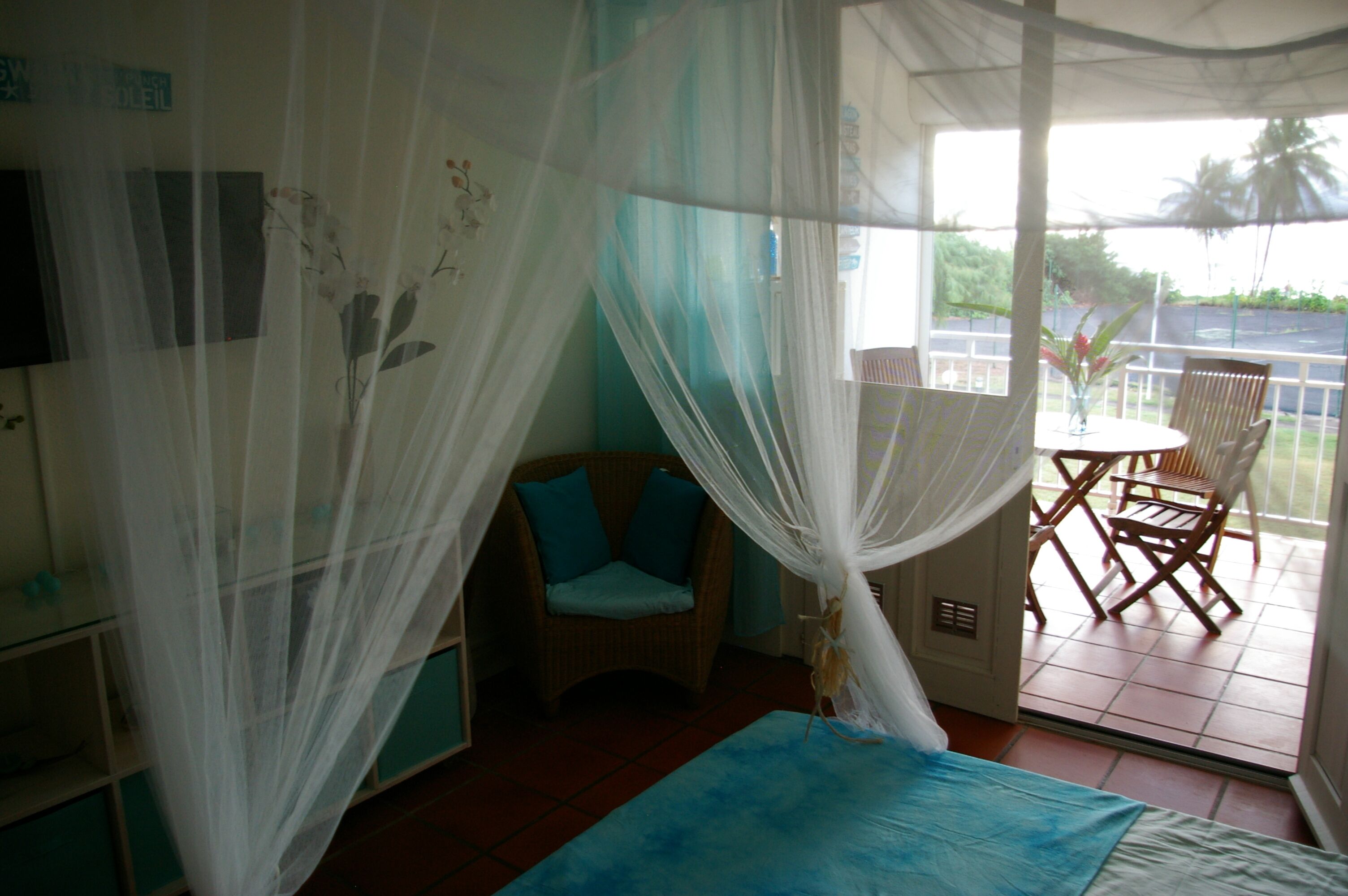 A room with a bed, a chair, a table, and a balcony with a view.