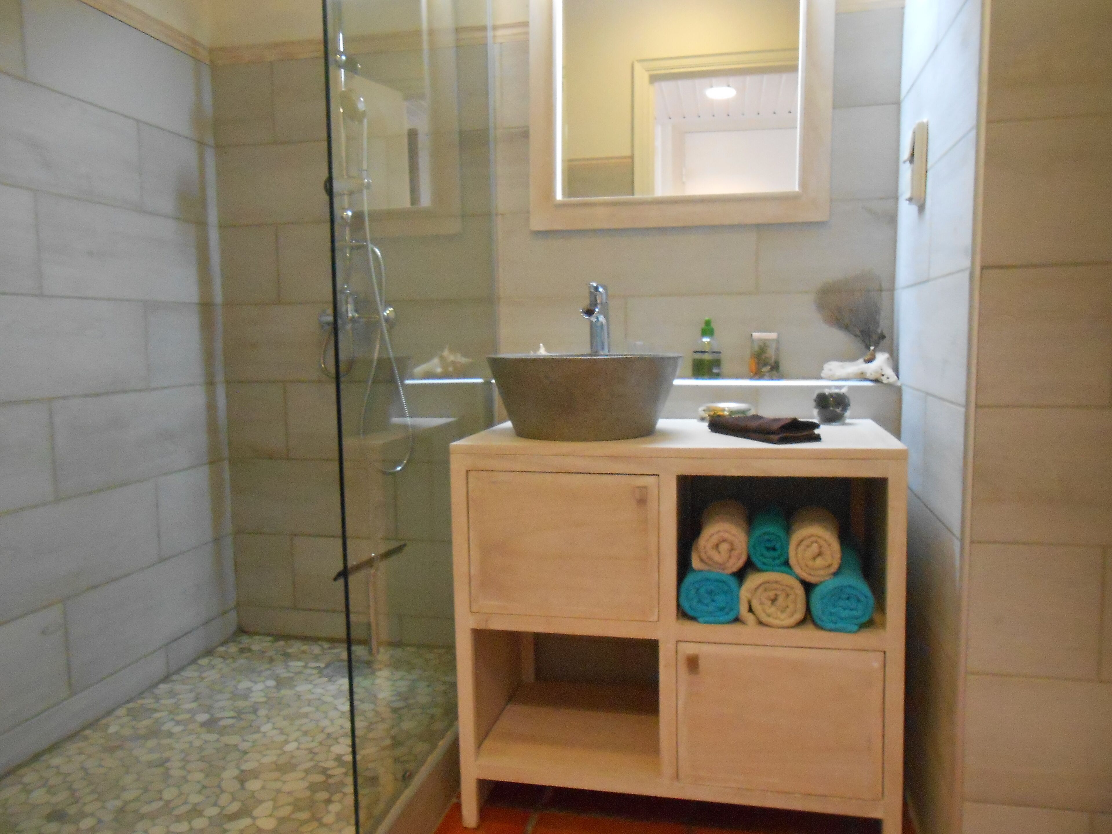 Un bany amb una cabina de dutxa de vidre, un tocador de fusta amb una tassa gran i tovalloles arremolinades amb cura.