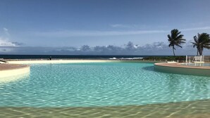 Una piscina cristalina con fondo de arena y vista al océano.