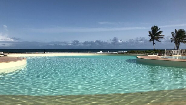 En klar pool med sandbund og havudsigt.