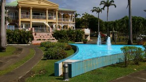 Et hotel med en stor swimmingpool, en springvand og en velholdt have med palmer.