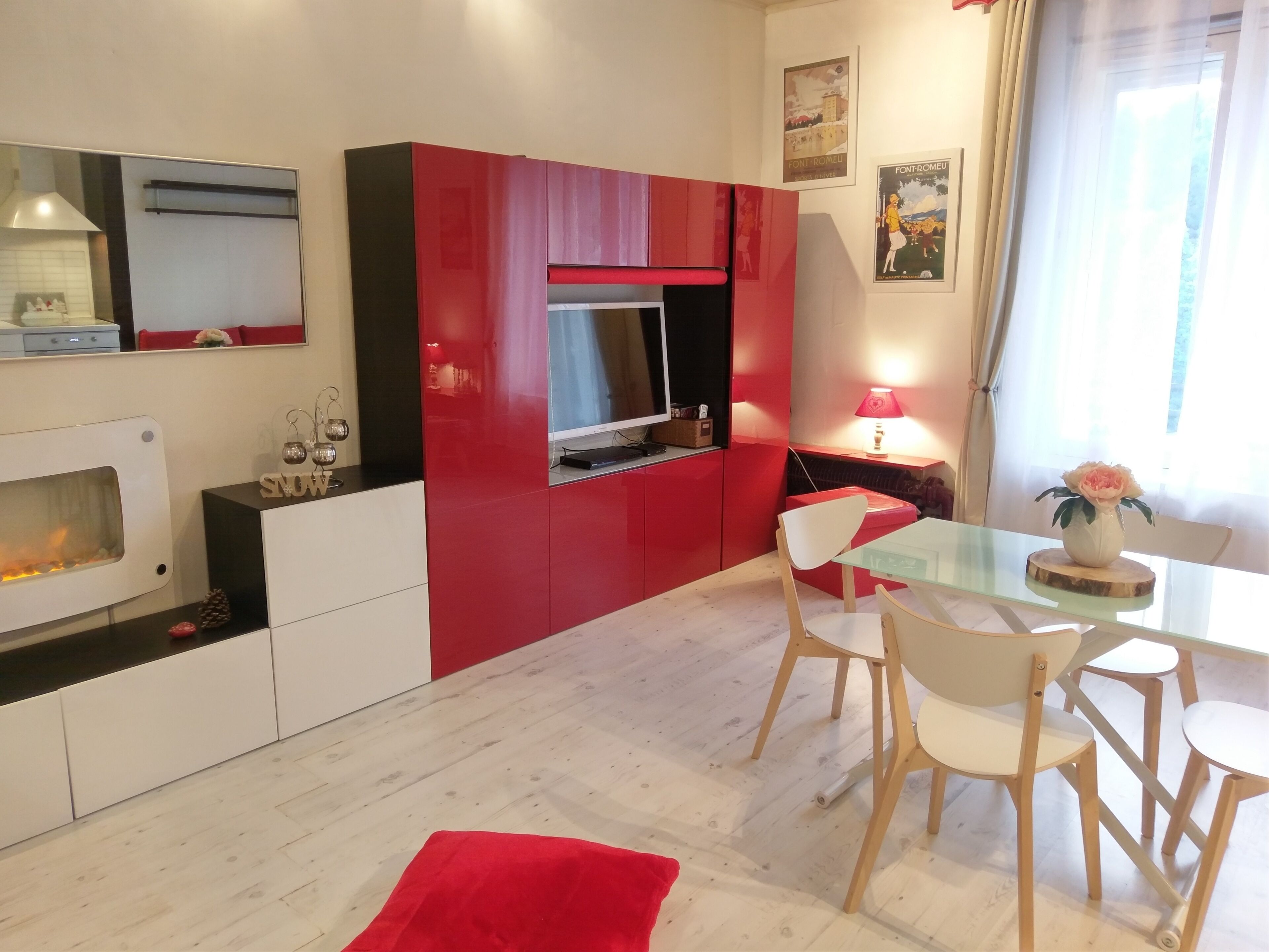 A modern kitchen with a red and white color scheme, a dining area with a glass table, and a fireplace.