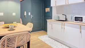 A modern kitchen with white cabinets, a dining table with wicker chairs, and a blue accent wall. - N&J - PLACE DU PIN - Port - Close Old Town (Niza)