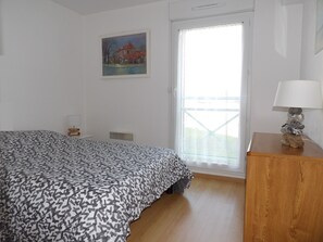 A bedroom with a bed, a painting, a window, and a lamp on a wooden nightstand.