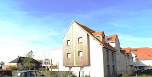 Un bâtiment à la façade en bois et au toit rouge, portant les indications « Portillon » et « Entrée principale » pour indiquer l’accès au parking et l’entrée principale.