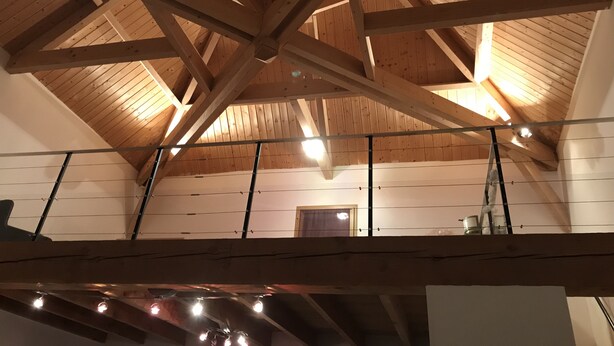 Una estructura de madera con techos altos, vigas a la vista y una escalera, que sugiere un espacio tipo desván o ático.