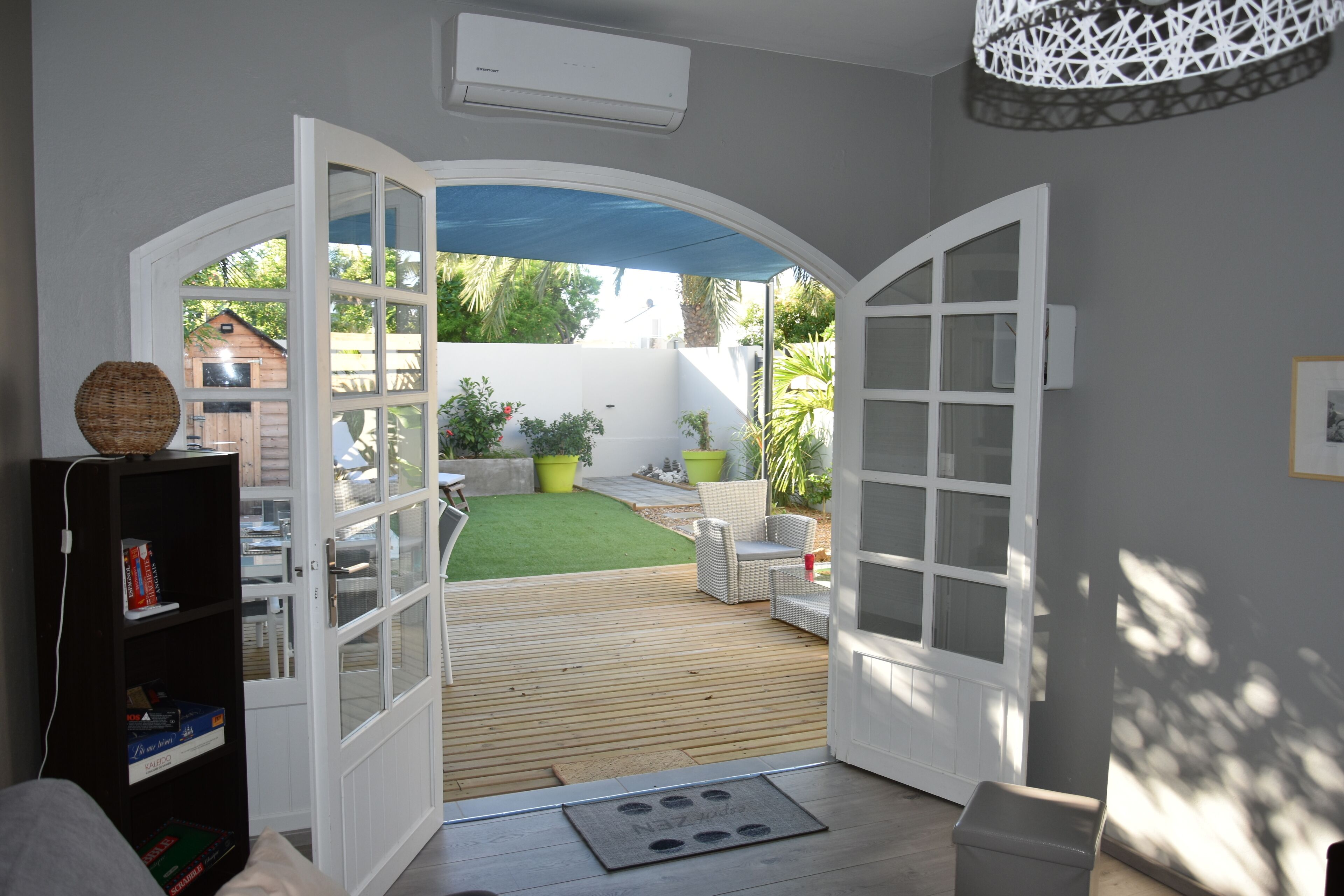 An open doorway leading to a patio with a wooden deck, outdoor furniture, and a green lawn.