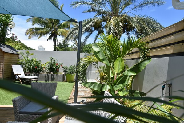 A patio area with a wicker chair, a potted plant, and a blue umbrella. - Charming outbuilding with large shaded terrace in private garden (l'Étang-Salé les Bains)
