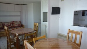 A dining area with a round wooden table and chairs, a sofa, and a TV mounted on the wall.
