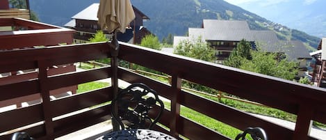 A balcony with a table and chairs, overlooking a mountainous landscape with buildings.