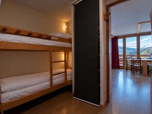 Ein Zimmer mit Etagenbetten, einer Schiebetür, einem Essbereich mit Stühlen und Bergblick durch große Fenster.