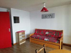 A cozy room with a wooden sofa, a red door, a small shelf, and a 'Happy' sign on the wall.