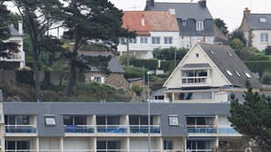 Un edificio costiero con diversi balconi, un'area di parcheggio e una spiaggia sabbiosa in primo piano.