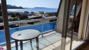 Un balcone con una porta vetrata, un tavolo rotondo e vista su un'area di parcheggio e un corpo d'acqua.