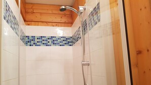 A shower with a chrome showerhead and hose, tiled walls with blue mosaic patterns, and wooden ceiling beams.
