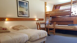 A room with two beds, a bunk bed, a wooden headboard, a framed picture, and a table with chairs.