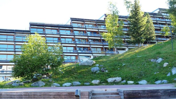 A modern building with multiple floors, large windows, and a sloped roof.