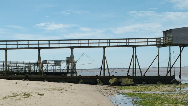 Una playa con un muelle de madera, redes de pesca y un pequeño edificio de madera.