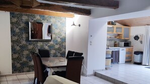 Un comedor con mesa y sillas, un sofá, una cocina con armarios y electrodomésticos, y un zócalo estampado.