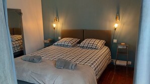 Una cama doble con un edredón estampado, dos mesitas de noche con lámparas y un espejo en la pared.