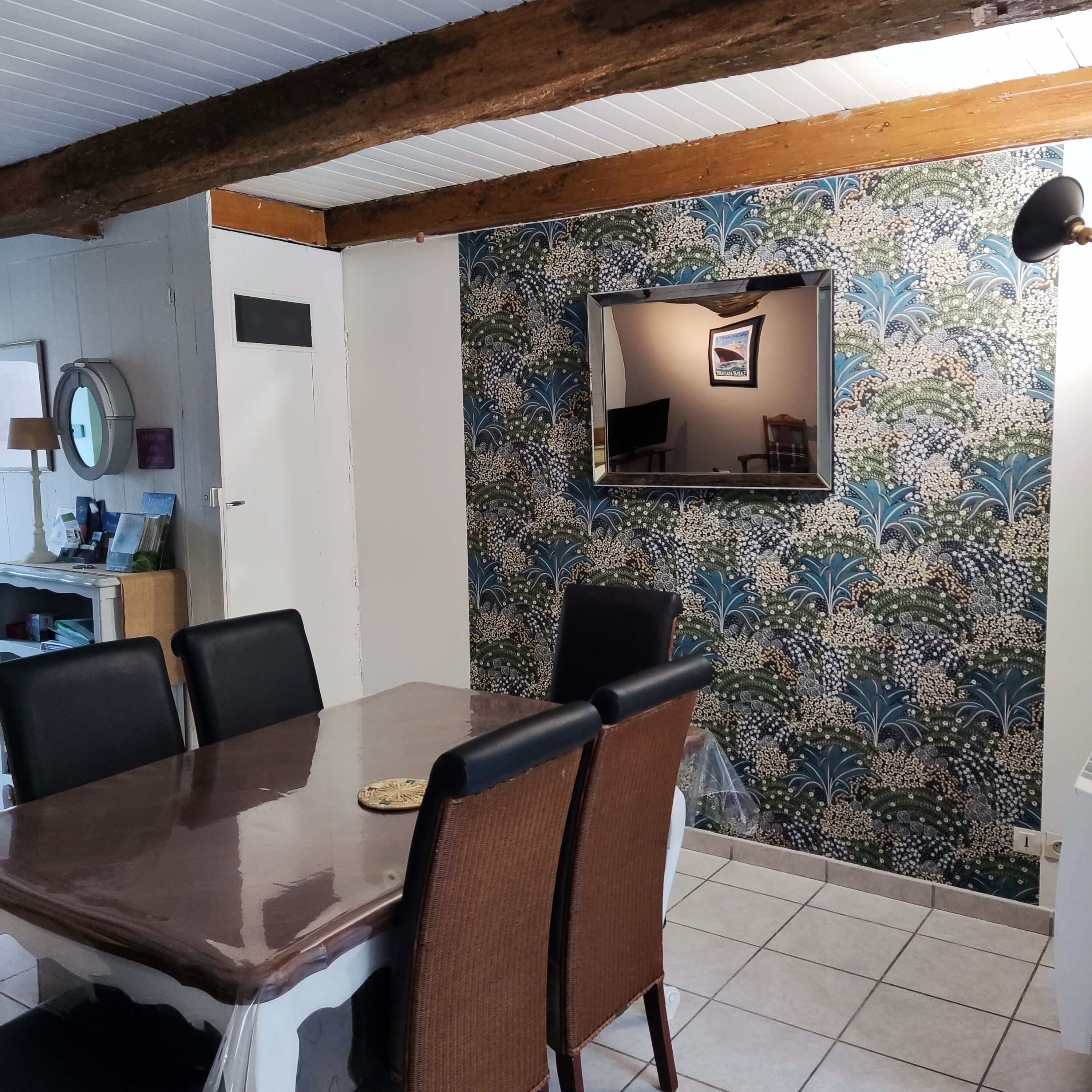 A dining area with a wooden table and chairs, a patterned wall, and a ceiling with exposed beams.