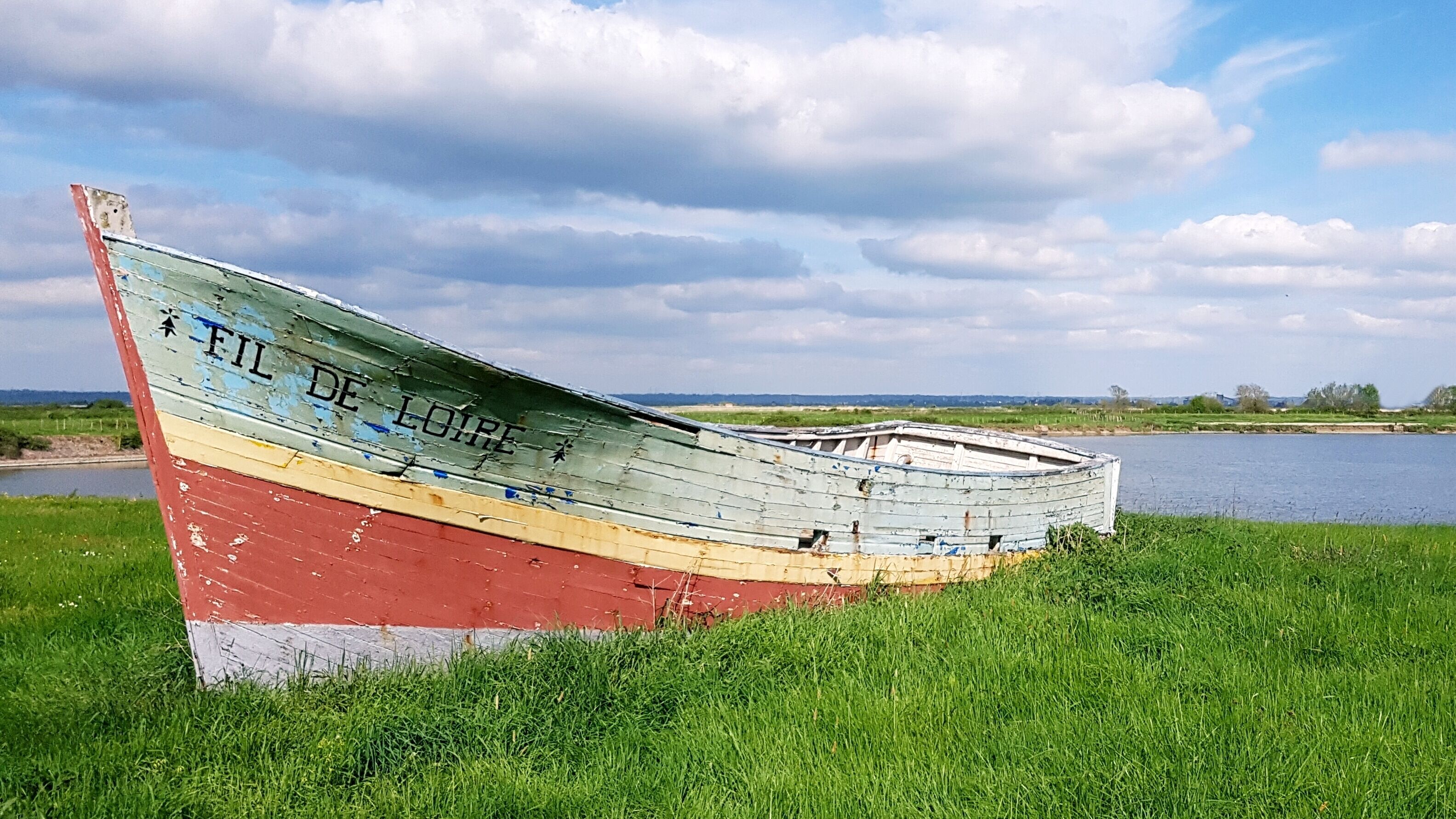 Um barco chamado "FIL DE LORE" repousa em uma margem gramada à beira da água.