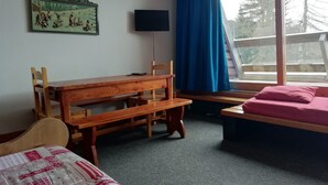 A room with a wooden desk, a bed with a pink bedspread, a television on the wall, and a window with blue curtains. - Large studio for 4 at Arc 1600 with wifi and pets allowed (Les Arcs 1600)