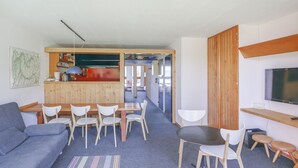 Un espace de vie compact comprenant un canapé, une table à manger, des chaises, un coin cuisine et un téléviseur.