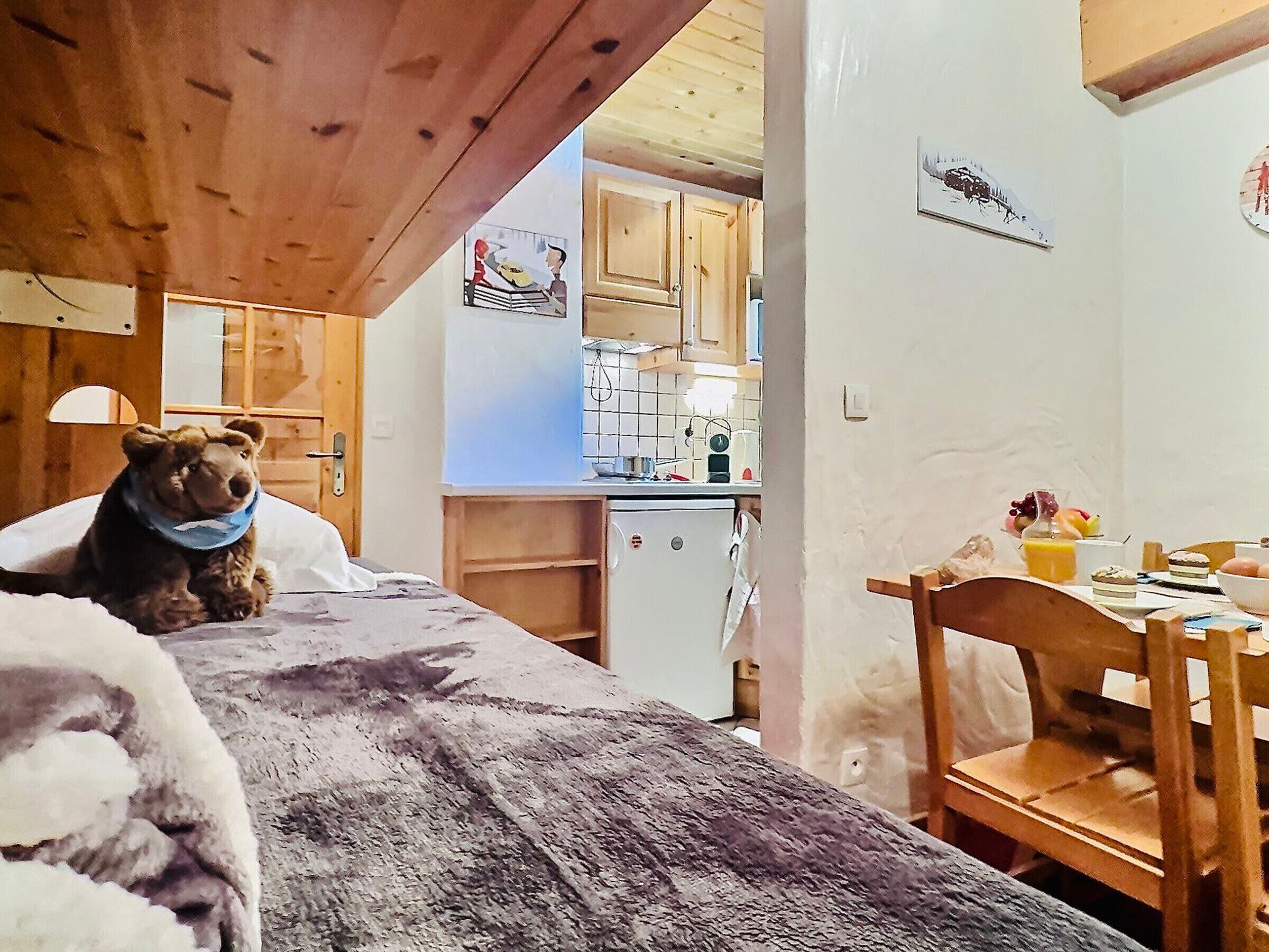 A cozy room with a bed, a wooden ceiling, a kitchen area, and a dining table with breakfast items.