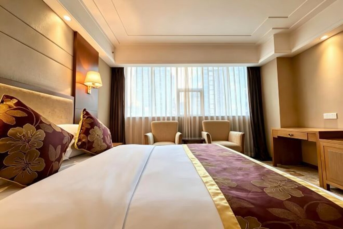 A hotel room with a large bed, two armchairs, a desk, and a window with curtains.
