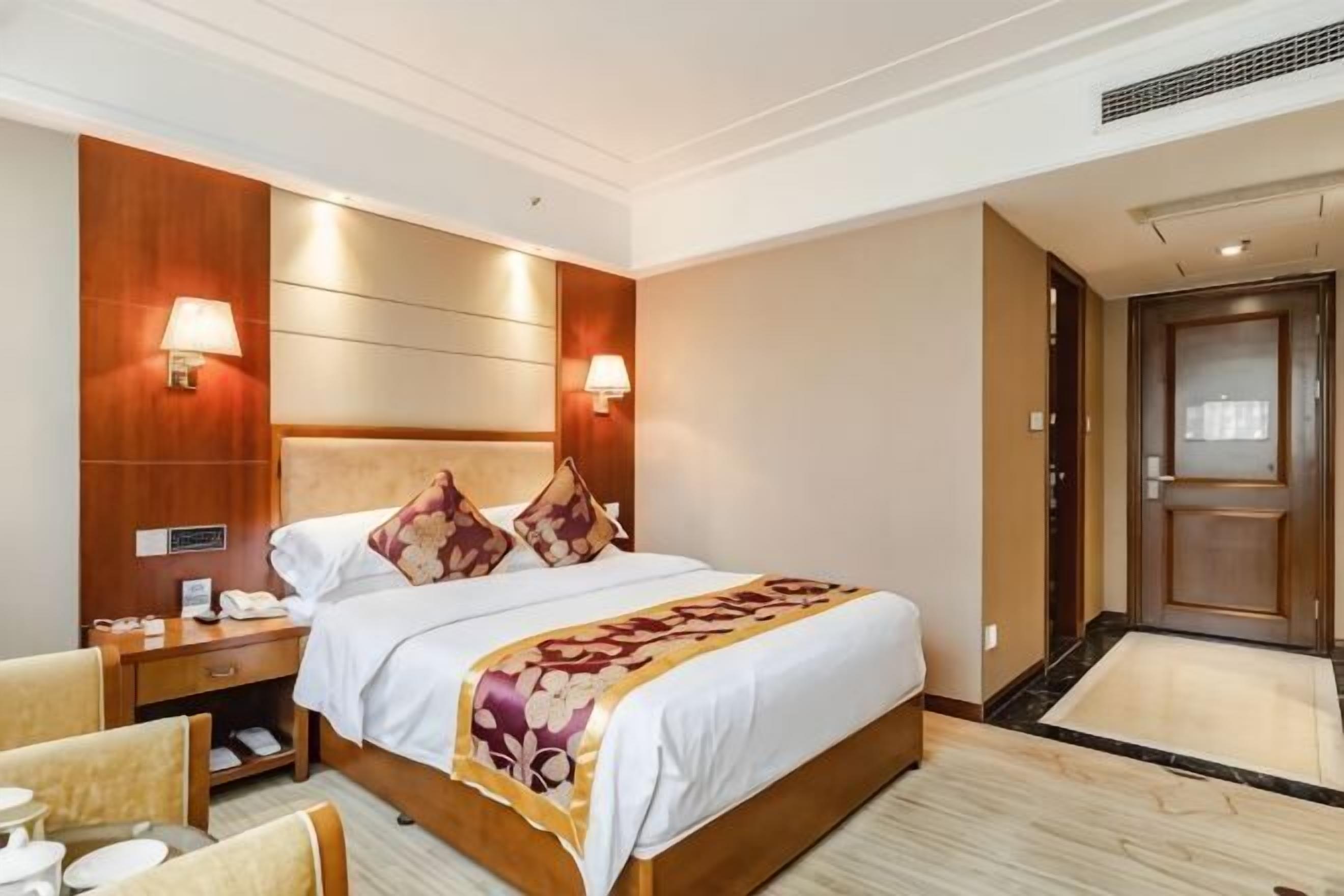 A hotel room with a large bed, bedside lamps, a nightstand, a chair, and a door.