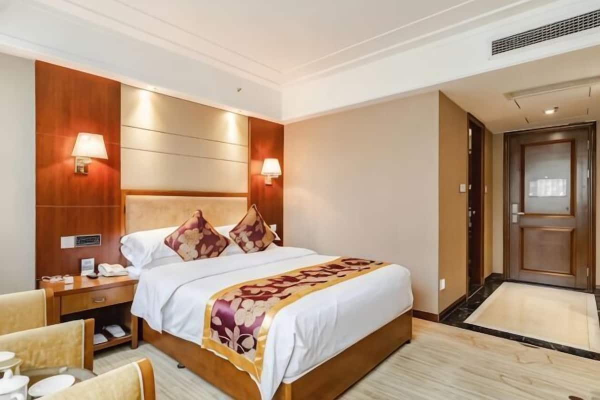 A hotel room with a large bed, bedside lamps, a nightstand, a chair, and a door.