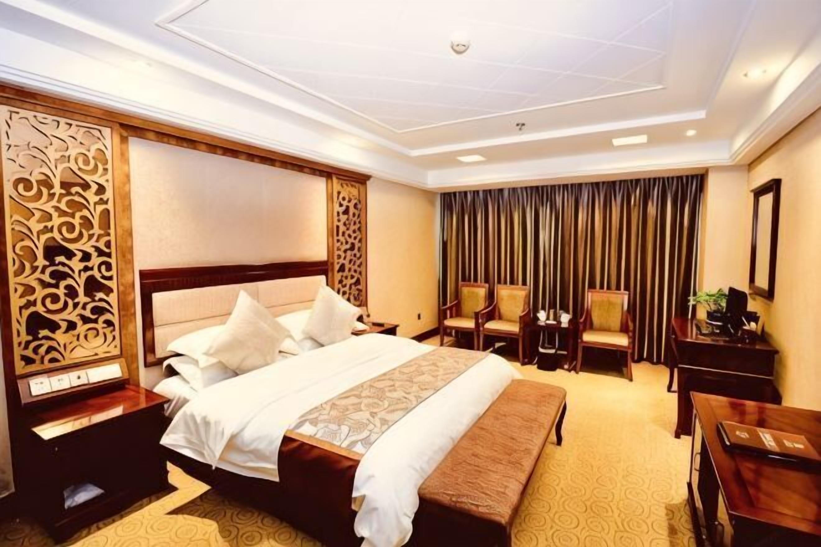 A hotel room with a large bed, a desk, two chairs, a bench, and a curtain.
