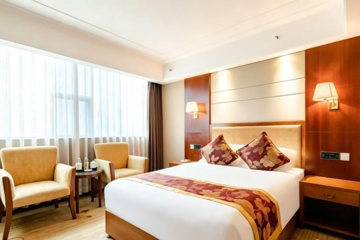Habitación de hotel con una cama grande, dos sillones, una mesita, una mesita de noche y una lámpara.