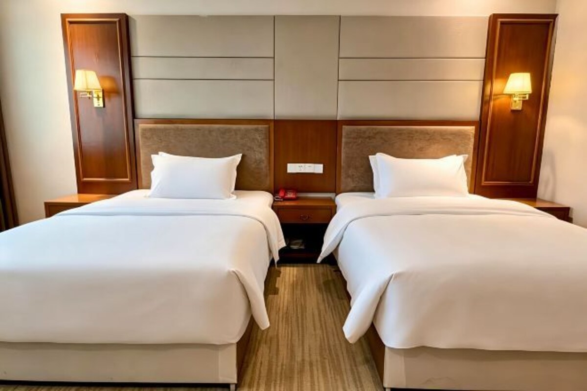 Una habitación de hotel con dos camas, cabecero de madera, lámparas de noche y suelo alfombrado.
