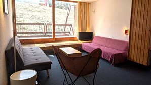 Et værelse med en sofa, en lænestol, et fjernsyn og et vindue med udsigt over en bakke.