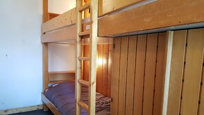 Et soveværelse med køjeseng, en trætraphængsel og en enkeltseng med blå madras.