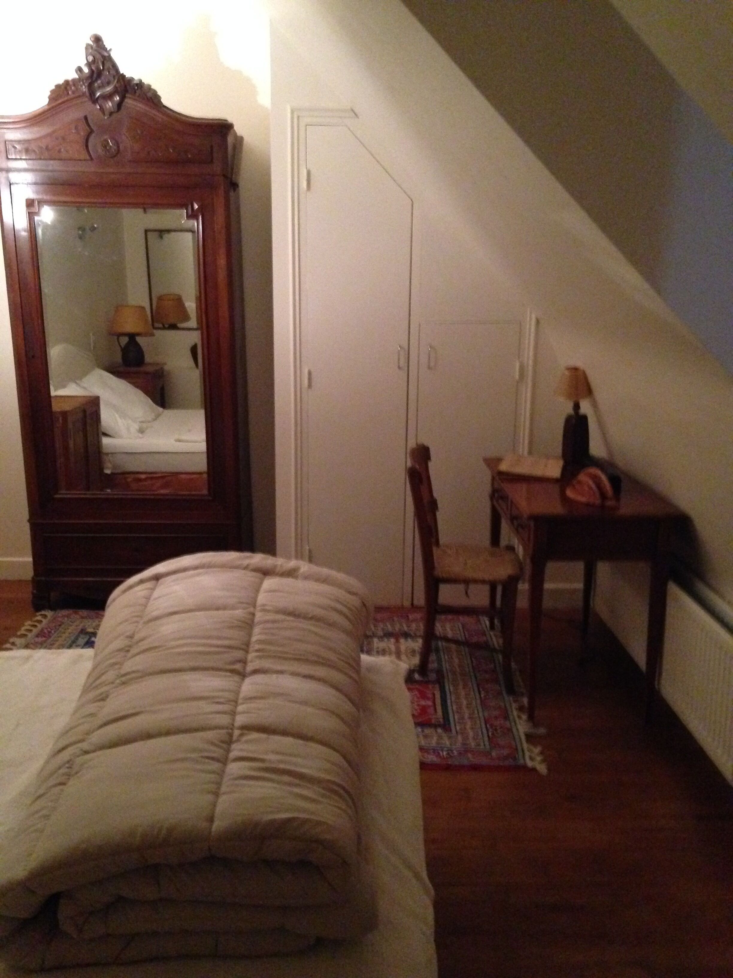 Quarto com cama, guarda-roupa de madeira, cadeira e uma pequena mesa com abajur.