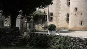 A stone building with a central tower, a statue in front, and a well-maintained lawn.