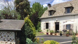 A stone building with a tiled roof, a garden with various plants and flowers, and a paved area with outdoor seating.