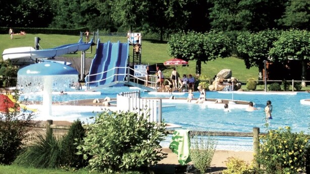 A swimming pool with a water slide, surrounded by trees and a grassy area.