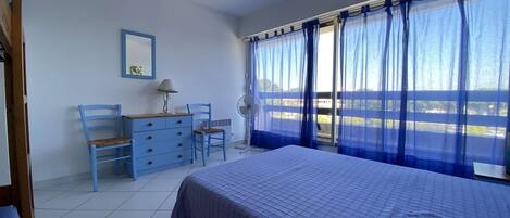 A bedroom with a bed, a desk, a chair, and a window with curtains.