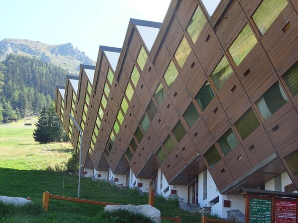 A row of chalet-style buildings with a symmetrical facade, set against a mountainous backdrop.