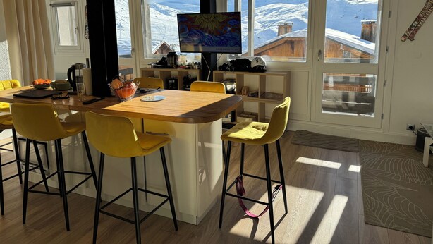 Una cucina moderna con isola in legno, sedie gialle e un'ampia finestra con vista innevata.