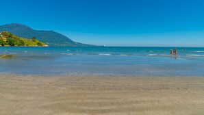 A beach with clear water, a mountain in the background, and a few people in the distance. - Pousada Vila Barequeçaba (São Sebastião)