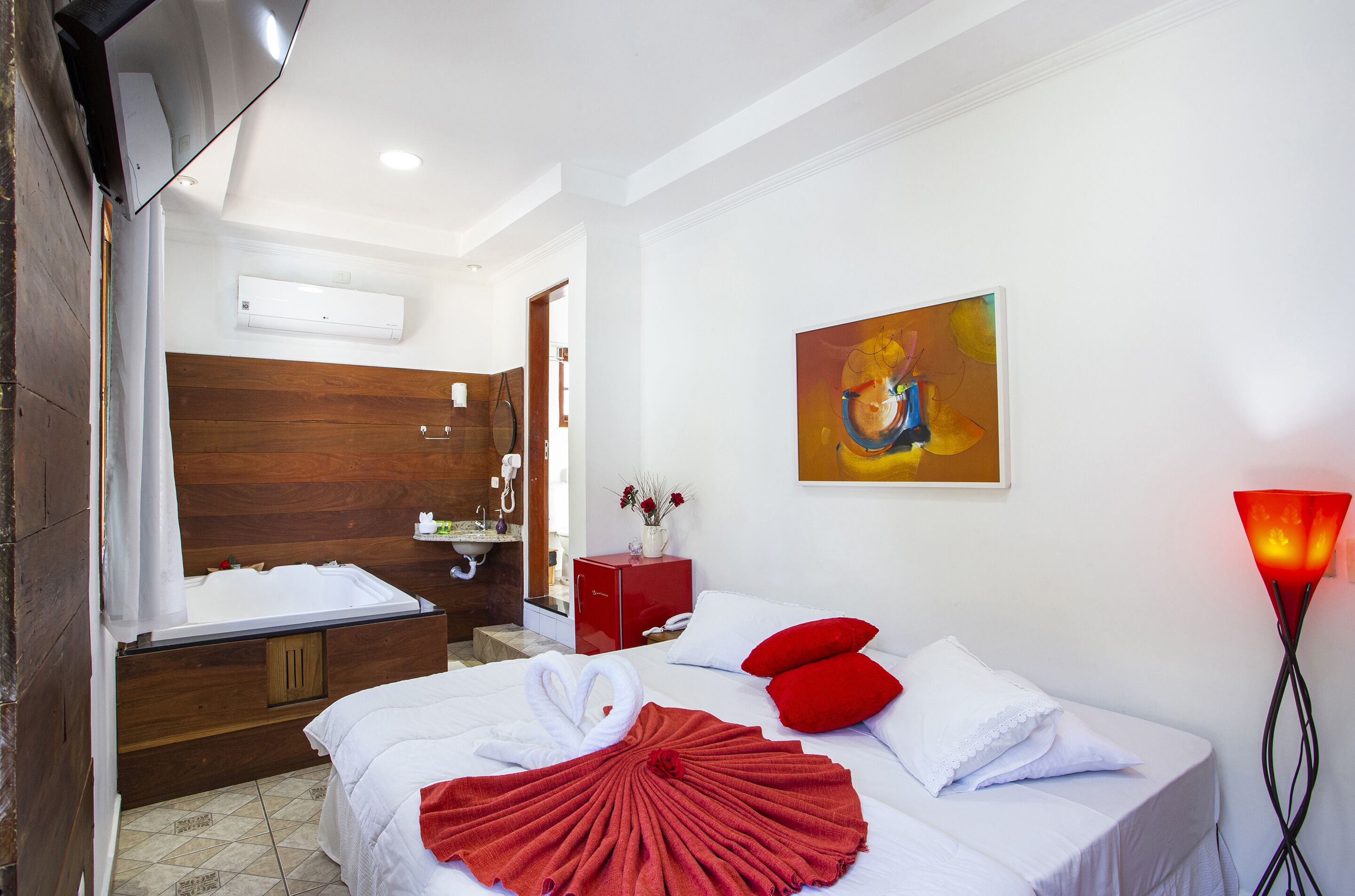A hotel room with a bed, a red cabinet, a painting, and a wall-mounted air conditioner.