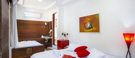 A hotel room with a bed, a red cabinet, a painting, and a wall-mounted air conditioner.