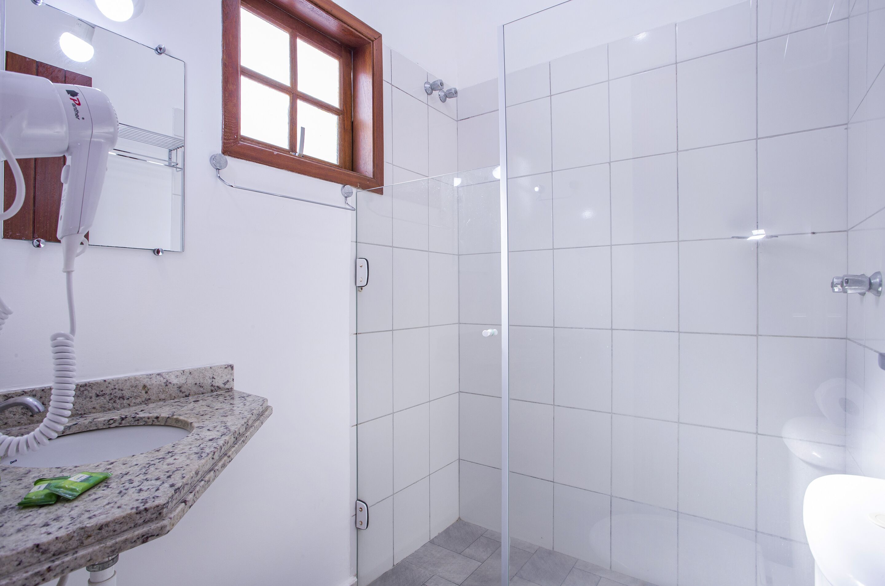 Un baño moderno con lavamanos de granito, secador de pelo, espejo y cabina de ducha de vidrio.