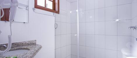 Un baño moderno con lavamanos de granito, secador de pelo, espejo y cabina de ducha de vidrio.